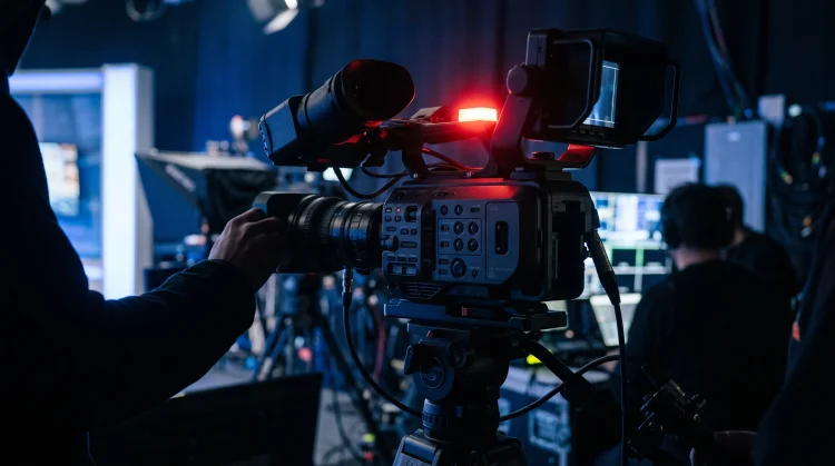 A professional broadcast camera in a darkened television studio.
