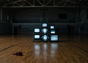 An empty high school gym with old TV monitors showing static and a red corsage on the floor.