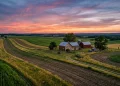 A wide view of a rural farmhouse and large acreage at sunset.