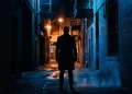 A conceptual silhouette of a man in a trench coat in a dark city setting.