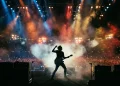 A silhouette of a musician performing on stage with bright spotlights in a large stadium.