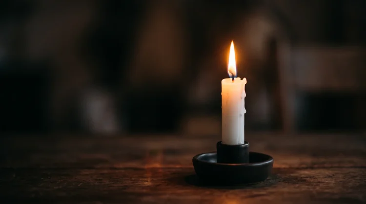 A soft glowing candle in a darkened room representing remembrance.
