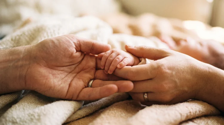 Conceptual image of parents holding a newborn's hand.