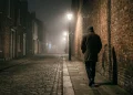 A silhouette of a person walking through a foggy alleyway at night.